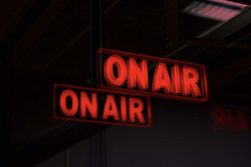 Pimeässä radiostudiossa hohtaa punaisella teksti, jossa lukee "On air".