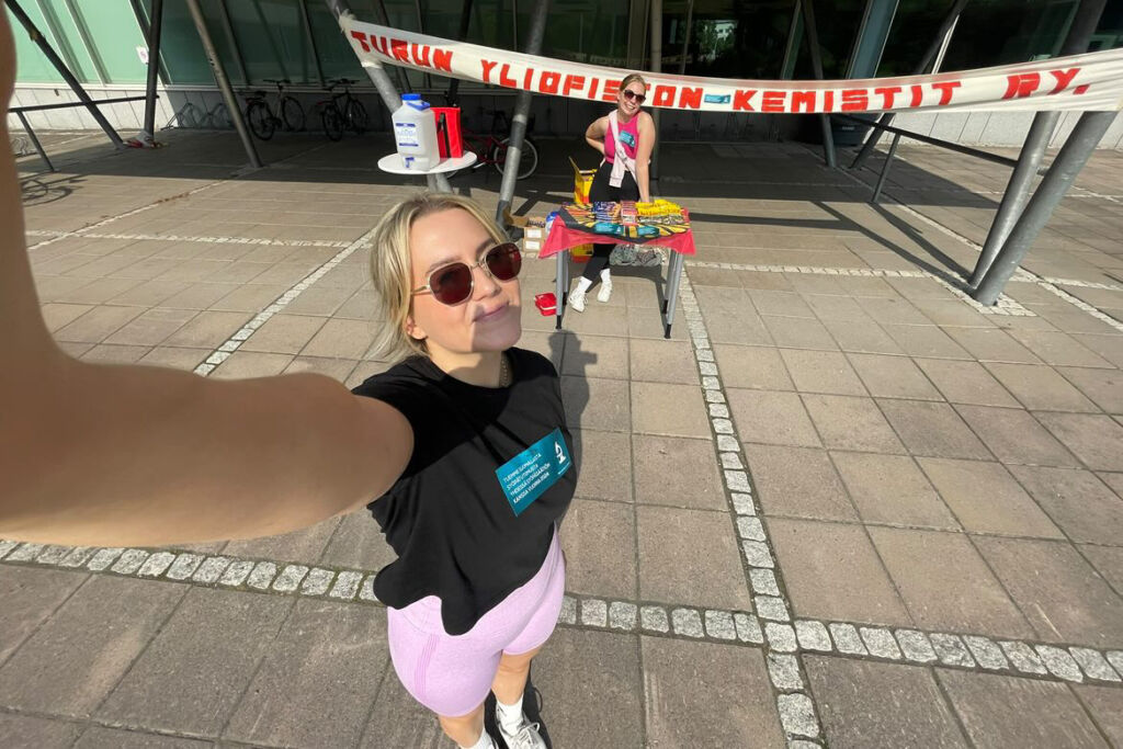 Kuvassa kaksi nuorta opiskelijaa. Taustalla näkyy ainejärjestön nimi.