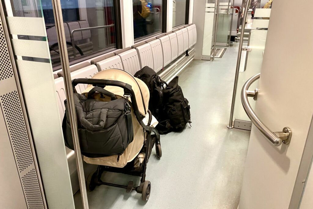 Lastenrattaat, joissa roikkuu hoitolaukku sekä reppu ja rinkka lattialla lähijunassa.