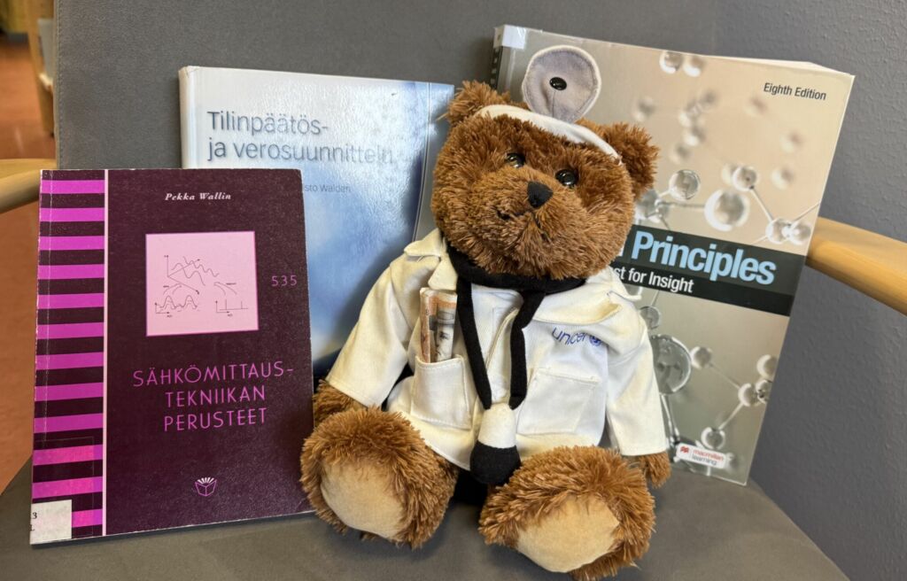 Kuvassa nalle lääkäritakissa ja eri alojen oppikirjoja.