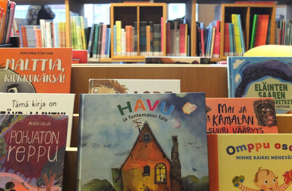 Runokuvakirja Havu ja Tuntematon talo kirjaston hyllyssä, vieressä muita kuvakirjoja.