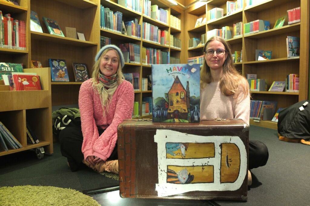 Kirjailija Veera Vähämaa ja kuvittaja Keanne van de Kreeke istuvat kirjaston lastenosaston lattialla. 